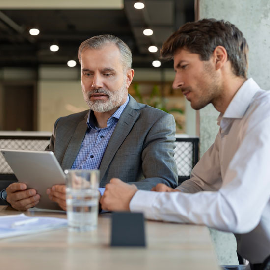 Dwóch mężczyzn przy stole w biurze, przegląda cyfrowe treści na tablecie, skupieni na dyskusji.