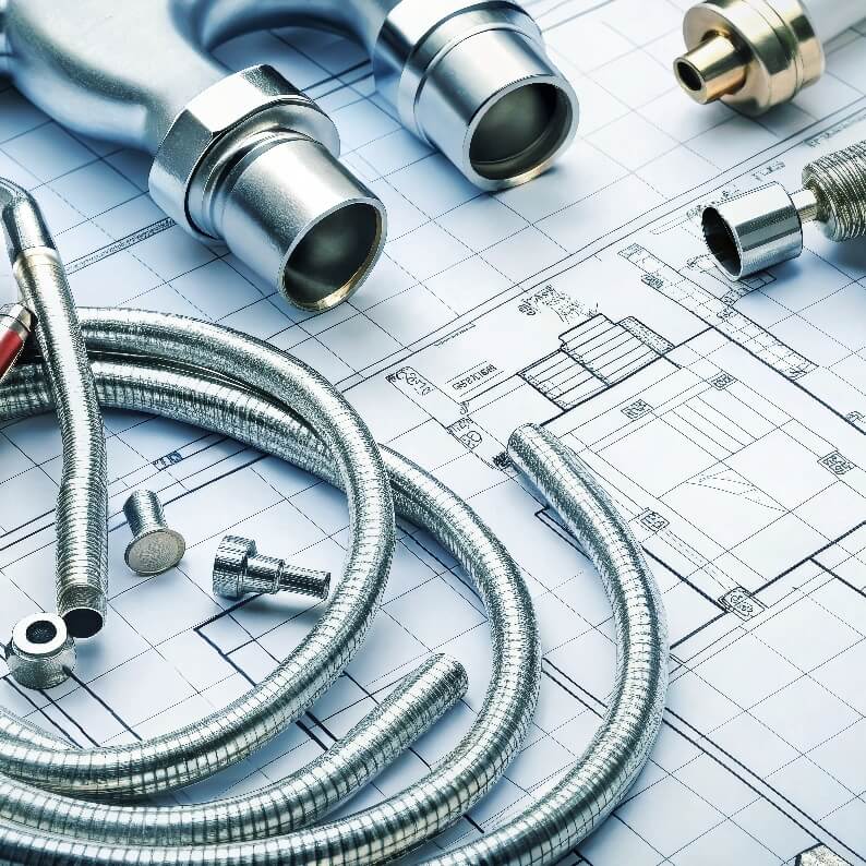 Rury metalowe i elementy hydrauliczne ułożone na planach technicznych, symbolizujące przygotowanie do instalacji.