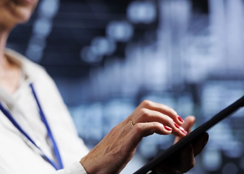 Osoba w białym stroju używa tabletu, dotykając ekranu na tle zamazanych, niebieskich świateł.