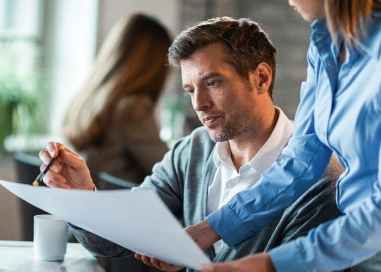 Mężczyzna skupia się na dokumentach, podczas gdy kobieta wyjaśnia coś, wskazując na kartkę.